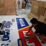 Seorang karyawan print merch sedang merapikan gudang cetak akrilik custom.